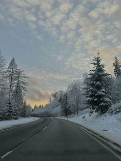 an empty road with snow on the ground and trees covered in snow, at dusk