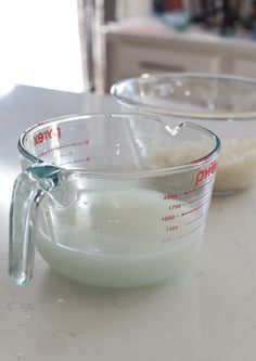 two measuring bowls filled with liquid on top of a white counter next to each other