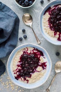 two bowls filled with oatmeal and blueberries next to silver spoons