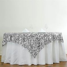 a table with silver sequins on it and white linen draped over the top