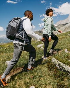 two young men hiking in the mountains with backpacks on their back and one holding his hand out