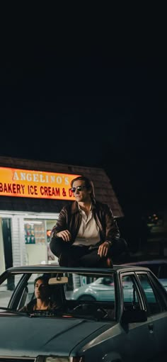 a man sitting on top of a car in front of a bakery