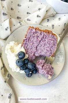 a piece of cake on a plate with blueberries and whipped cream next to it