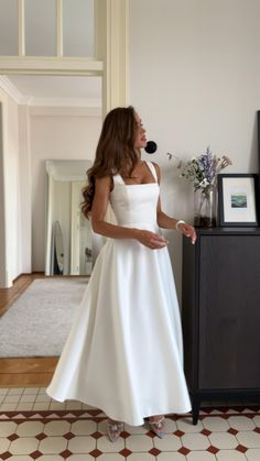 a woman in a white dress standing next to a dresser