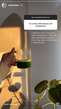 a person holding a glass with green liquid in it next to a potted plant