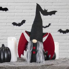 a black and red halloween gnome sitting on top of a table next to two candles