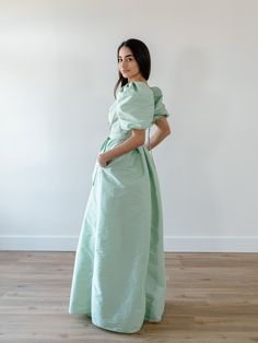 a woman in a green dress standing on a wooden floor with her hands on her hips