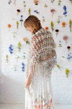 a woman is standing in front of a wall with flowers on it and she has her back to the camera