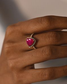 a woman's hand with a red heart shaped diamond ring on her left hand