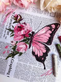 a pink butterfly sitting on top of a newspaper next to some crayons and flowers