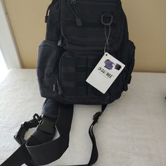 a black backpack sitting on the floor next to a white wall with a tag hanging from it