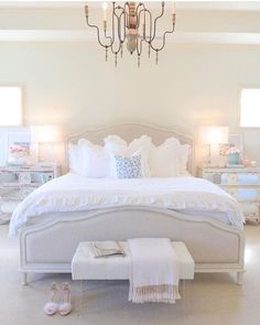 a bedroom with a chandelier and white bedding, shoes on the floor