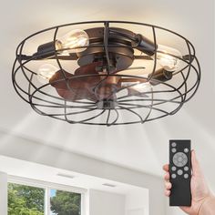 a person holding a remote control in front of a ceiling fan with lights on it