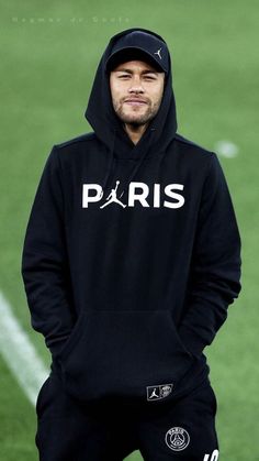 a man wearing a hoodie standing on a soccer field with his hands in his pockets