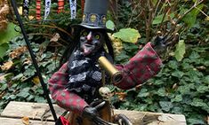 a scarecrow with a hat and cane is sitting on a bench in the woods