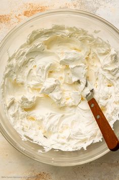 a glass bowl filled with whipped cream and a wooden spatula on top of it