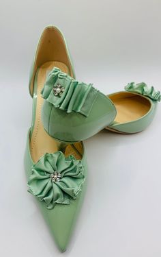 pair of green shoes with bows on the toe and heel, sitting on top of each other