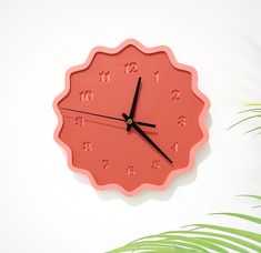 a pink clock with numbers on the face and palm leaves in front of white wall