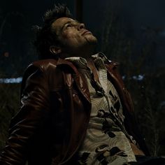 a man in a leather jacket is sitting on the ground and looking up at something