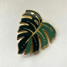 a green and gold leaf brooch sits on a white surface