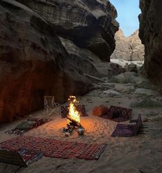 a campfire in the middle of a desert with blankets and rugs around it