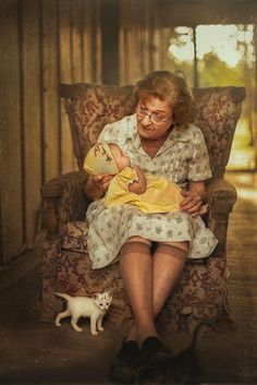 an older woman holding a baby while sitting in a chair next to a white cat