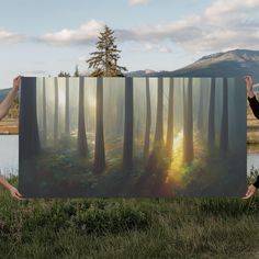 two women holding up a large painting in front of a body of water with trees on it