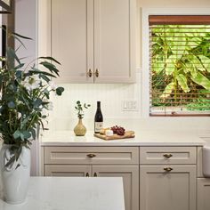 a kitchen with white cabinets and green plants in the window sill next to it