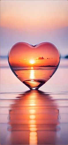 a heart shaped object sitting on top of a body of water with the sun setting in the background