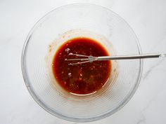 a glass bowl filled with sauce and whisk on top of a white counter