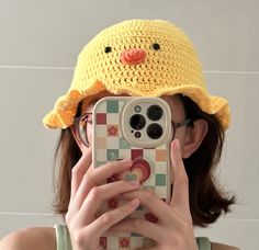 a woman taking a photo with her cell phone wearing a crocheted duck hat