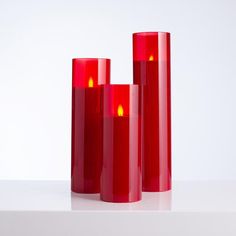 three red candles sitting next to each other on top of a white table with one candle lit