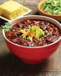 a red bowl filled with chili next to two bowls of salad and bread on a table