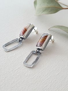 A pair of small rectangular Laguna Lace agate pairs are set in fine and sterling silver. Colorful bands of deep red, bright gold and pale lavender move in wavy stripes through the stones: a beautiful desert sunset palette. Silver rectangles textured with fused silver dust mirror the shape of the agates, and dangle freely below the stones. A window cut behind the stones allows you to view the backside of these unusual natural agates. The silver is oxidized and given a brushed finish to give a beautiful contrast between the stones and the textured metal. The sterling silver posts measure 9mm in length and have a bullet clutch back that is easy to grip and comfortable to wear. These one of a kind stud earrings measure 1 1/2" in length, and 3/8" wide. They are ready to ship! Rectangular Polished Earrings For Gift, Rectangular Polished Finish Earrings For Gift, Rectangular Polished Earrings For Gifts, Modern Earrings With Rectangular Stone Gift, Modern Earrings With Rectangular Stone For Gift, Modern Rectangular Stone Earrings For Gifting, Contemporary Sterling Silver Rectangular Jewelry, Contemporary Rectangular Sterling Silver Jewelry, Elegant Rectangular Agate Jewelry