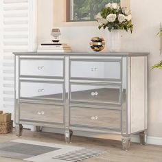 a silver and white dresser with flowers on top in a room next to a window