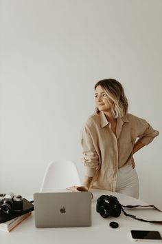 a woman standing in front of a laptop computer on a table with other items around her