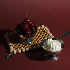 a bowl of whipped cream with cherries in the background on a red tablecloth