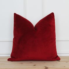 a red pillow sitting on top of a wooden floor next to a white painted wall