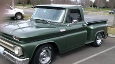 an old green pickup truck parked in a parking lot