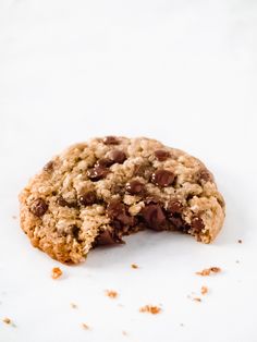 an oatmeal cookie with chocolate chips is half eaten on a white surface