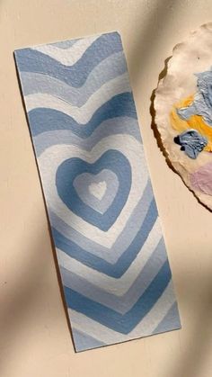 a blue and white paper plate next to a heart - shaped piece of art on a table