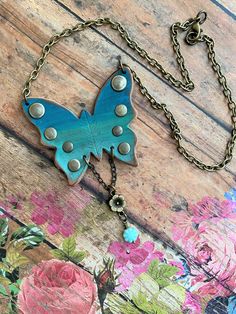 a blue butterfly is hanging from a chain on a wooden surface with pink flowers in the background