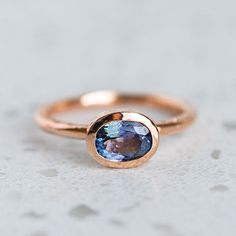 a rose gold ring with an oval blue topazte in the center on a white surface