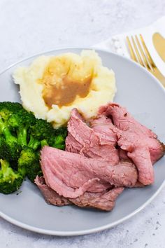 a plate with meat, mashed potatoes and broccoli on it next to a fork