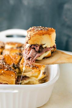 a roast beef sandwich is being lifted from a casserole dish by a wooden spoon