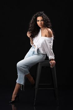 a beautiful woman sitting on top of a stool wearing high heeled shoes and a white shirt