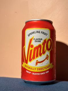 an unopened can of soda sitting on a blue tablecloth in front of a pink wall