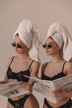 two women in bathing suits are looking at a newspaper while wearing towels on their heads