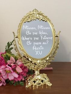 a mirror sitting on top of a wooden table next to pink flowers and a vase