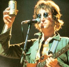 a man holding up a can while standing in front of a microphone and playing an electric guitar